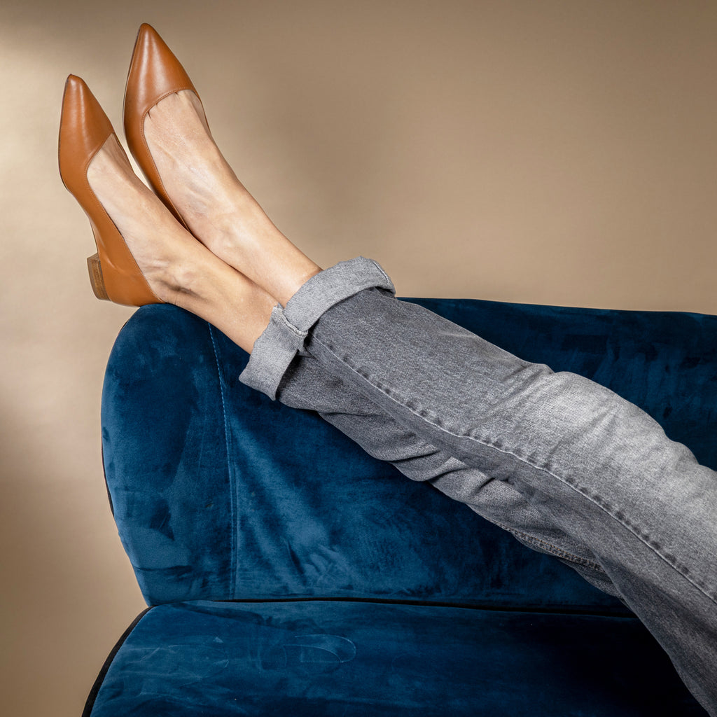 Ballerines pointues en cuir camel portées avec un jean, jambes croisées sur canapé bleu